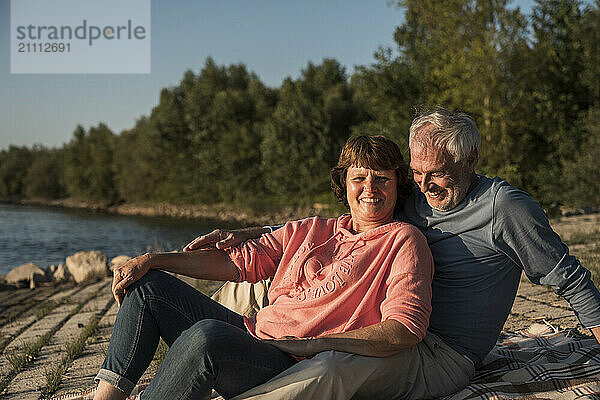 Happy senior couple sitting near river on sunny day