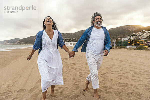 Cheerful couple holding hands and walking on sand