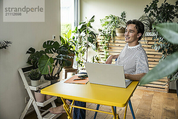 Smiling young businessman sitting at desk with laptop in home office