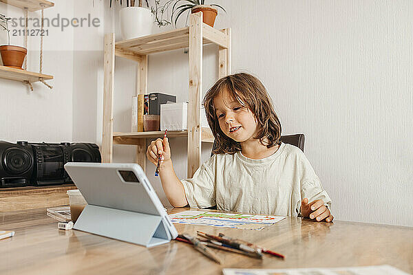 Cute boy sitting near table and learning painting on Digital PC at home