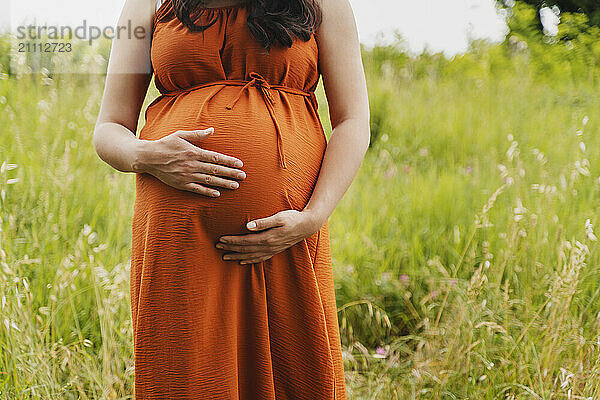 Pregnant woman with hands on stomach standing in grass