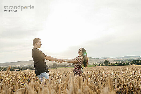 Happy couple holding hands and dancing in spikelet field