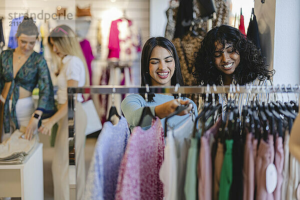 Happy friends selecting dress from rack at fashion store