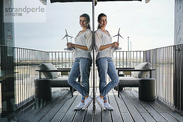 Portrait of pretty blonde leaning on glass wall with model of wind turbine in hands