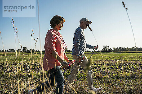 Senior man and woman walking with hiking poles on meadow