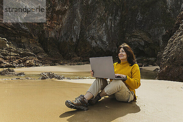 Smiling freelancer sitting and using laptop at beach