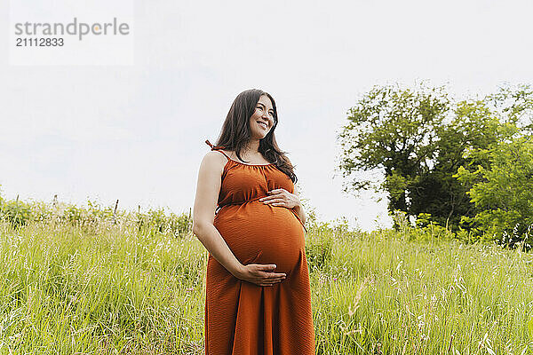 Happy pregnant woman standing in grass area