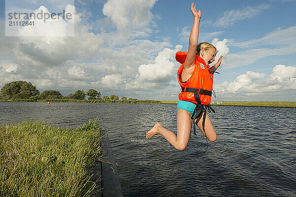 Girl wearing life jacket jumping in lake