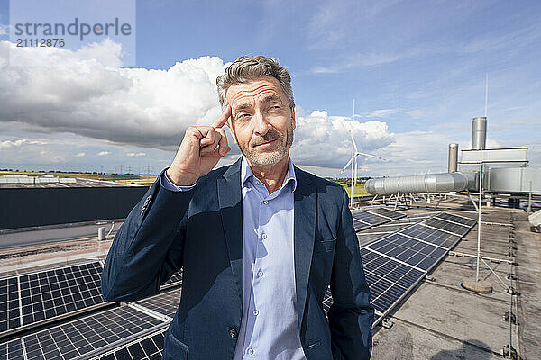 Mature businessman touching temple standing on rooftop with solar panels