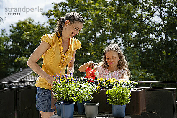 Smiling woman with daughter watering flowers on balcony