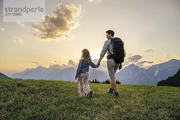 Father exploring with daughter in meadow at sunset