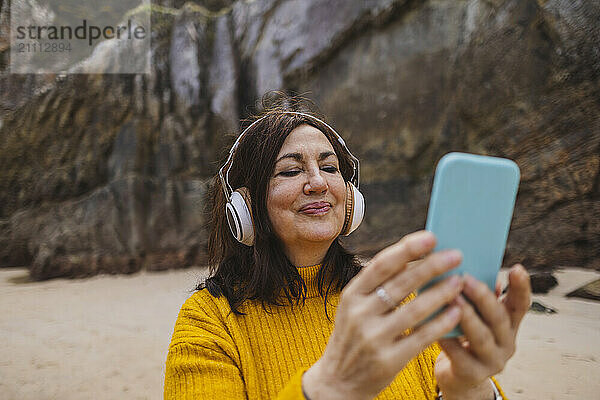 Smiling senior woman using smart phone and listening to music on beach