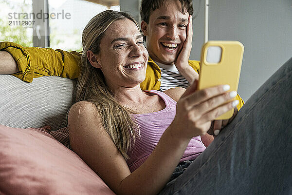 Happy blond woman using smart phone with boyfriend at home