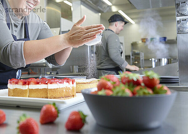 Smiling chef sprinkling powdered sugar on cake in restaurant