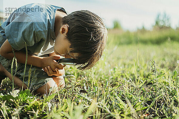 Boy looking at grasses through magnifying glass in forest