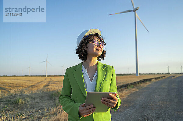 Thoughtful engineer holding tablet PC standing in wind farm