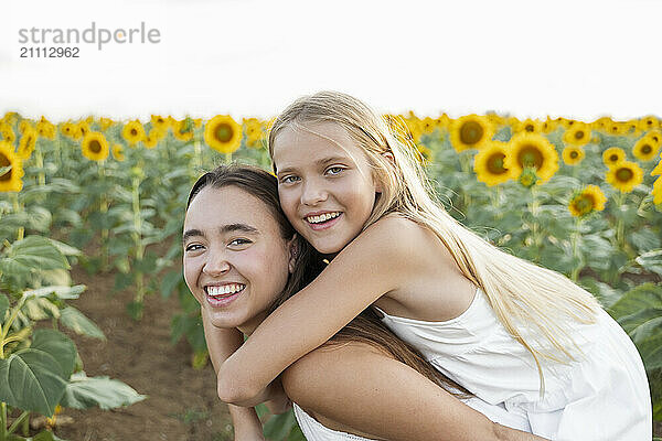 Happy woman piggybacking sister in sunflower field