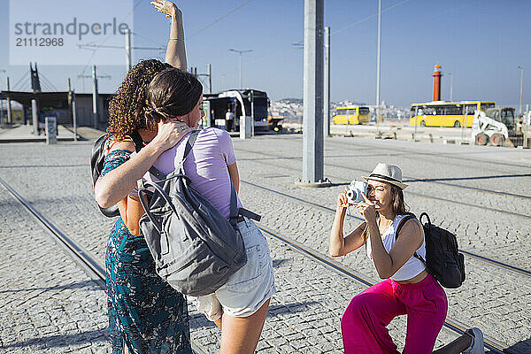 Woman wearing hat photographing friends with camera on tram tracks