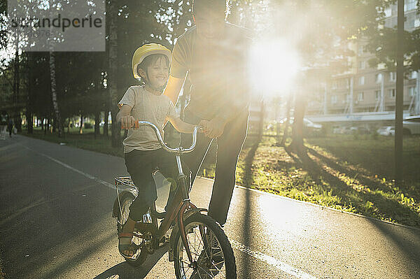 Father helping son in riding bicycle on sunny day