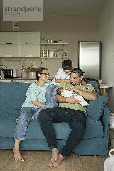 Cheerful family with new born baby sitting on sofa at home