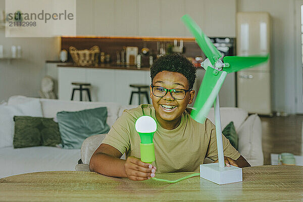 Happy boy powering light bulb through wind turbine model at home