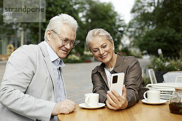 Happy senior couple taking selfie using smart phone at sidewalk cafe