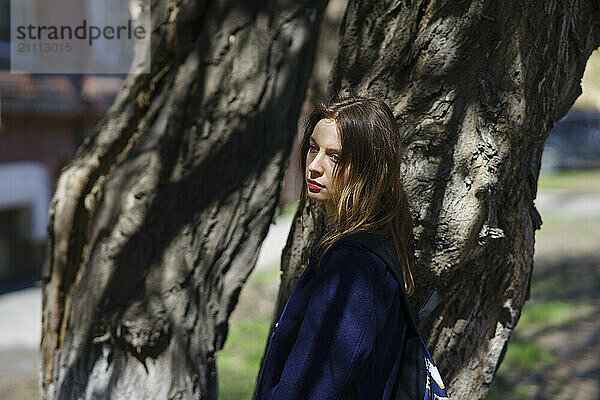 Sad woman standing by tree at sunny day