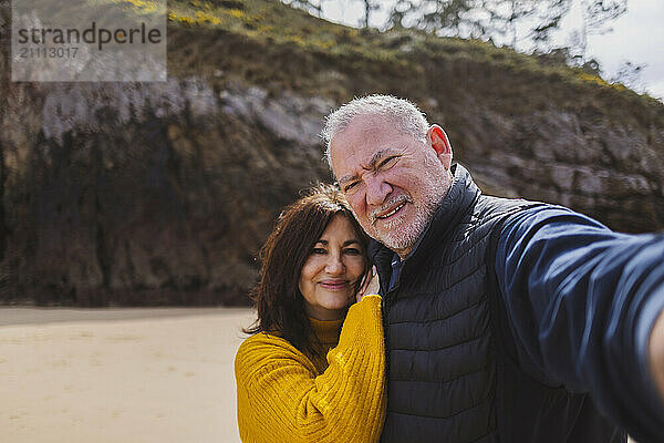 Smiling senior couple taking selfie at beach