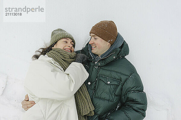 Smiling man lying down with woman on snow in winter