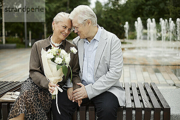 Happy woman holding bouquet and sitting on bench in street