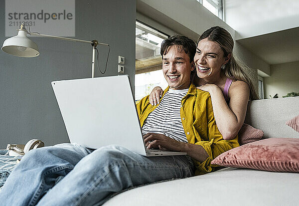 Happy woman leaning on boyfriend using laptop on sofa at home