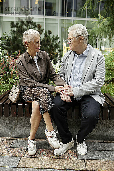 Senior couple sitting near building at street