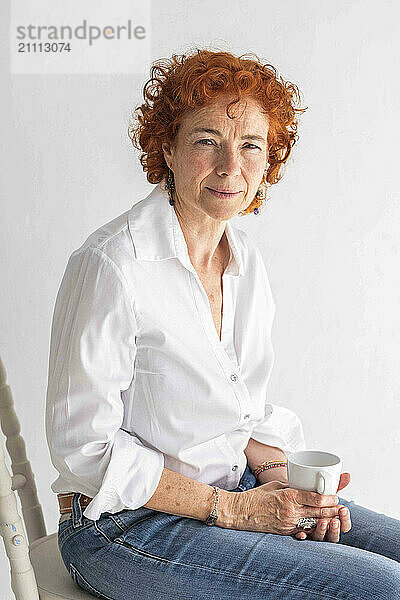 Redhead woman sitting and holding coffee mug against white background