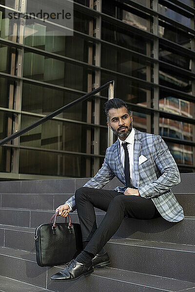 Businessman with suitcase sitting on stairs outside office building