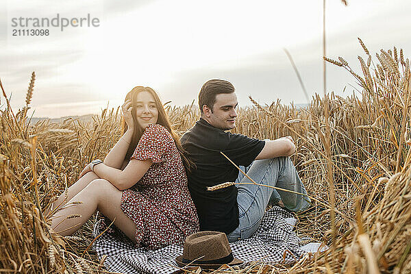 Happy young couple sitting back to back in dry field