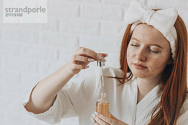 Teenage girl applying serum from a dropper bottle during her skincare routine at home.