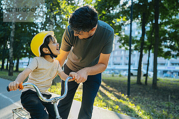 Cute boy practicing cycling with father on road