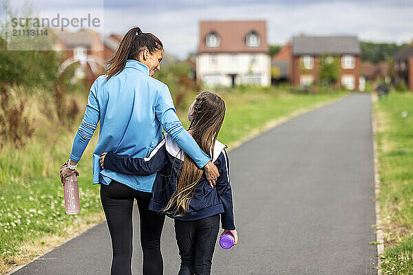 Mother and daughter walking with arms around on footpath