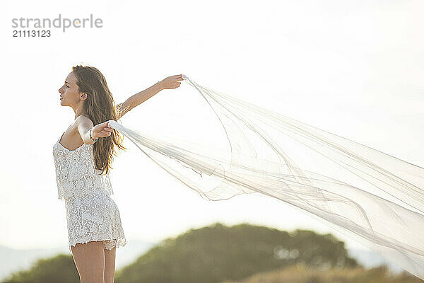 Young woman standing and holding cloth at beach