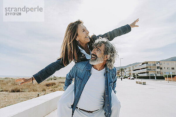 Happy senior man piggybacking carefree woman to gthe beach