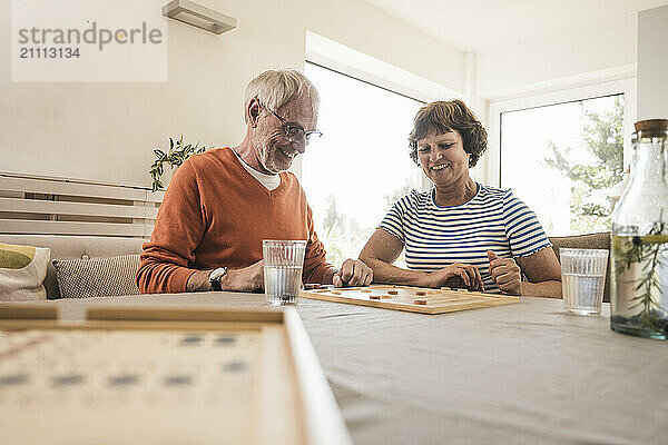 Happy senior couple playing board game on table at home