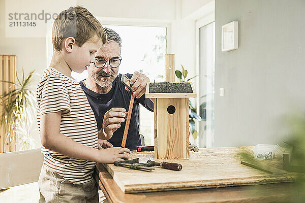 Grandfather making wooden birdhouse with grandson at home