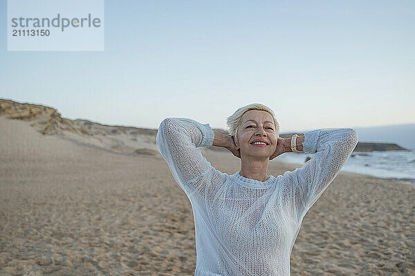 Smiling mature woman with hands behind head at beach