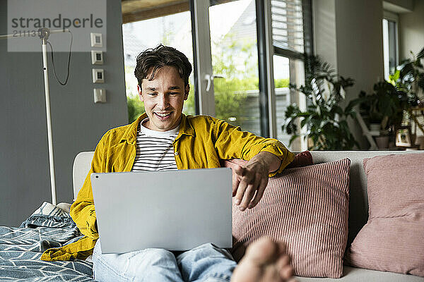 Smiling young man using laptop on sofa at home