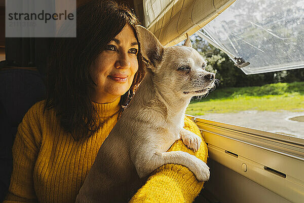 Thoughtful senior woman with dog looking out of window from motor home