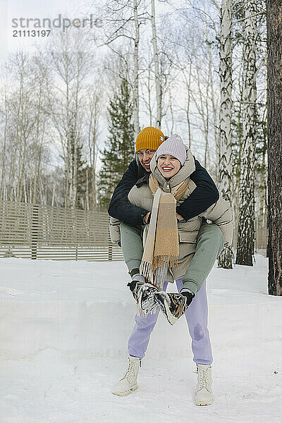 Happy woman piggybacking man on snow in winter