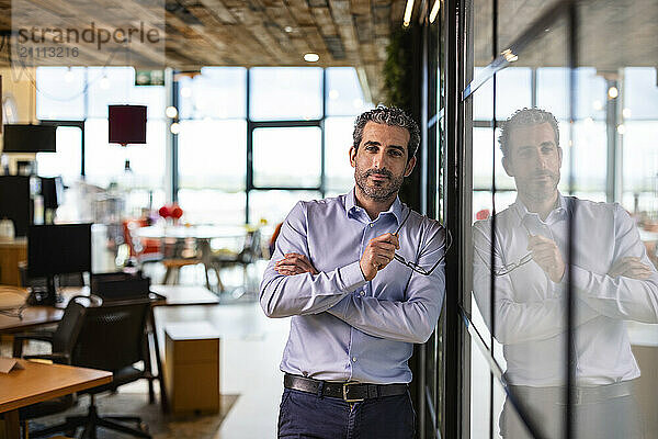 Businessman holding eyeglasses and leaning n wall at co working space