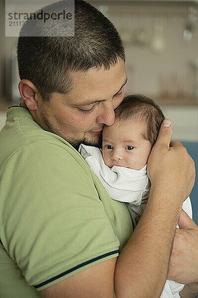 Happy father carrying baby in arms at home