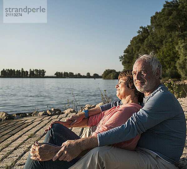 Senior couple sitting together near river on sunny day