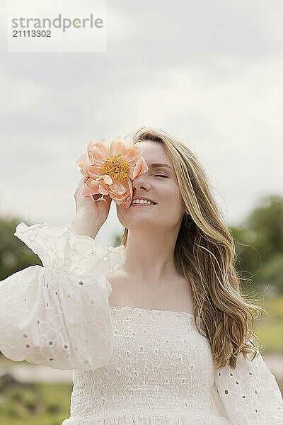 Beautiful woman covering eye with peony flower at garden